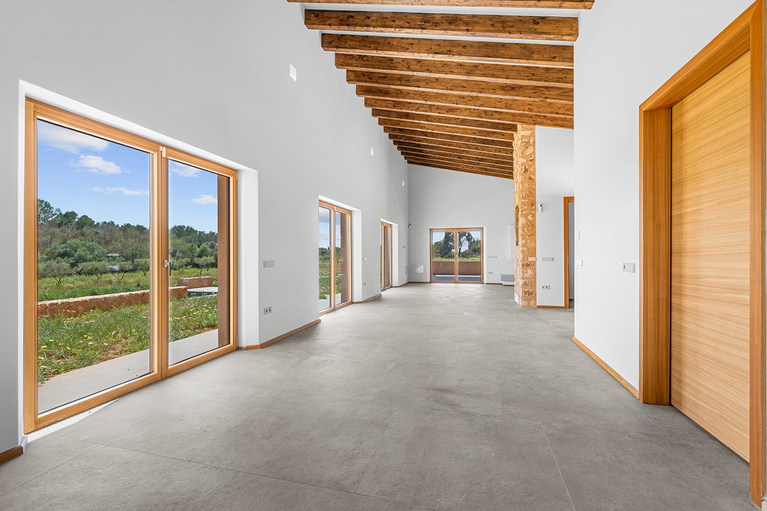 Espacio abierto de salón y pasillo con ventanales continuos y vigas vistas