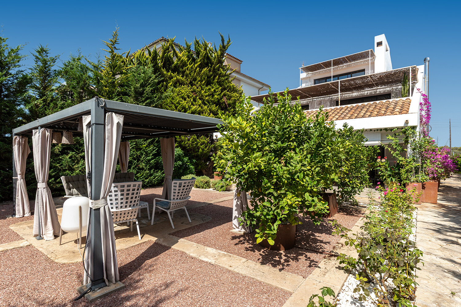 Amplio jardín mediterráneo con pérgola sombreada, distintas zonas de descanso y vistas a la vivienda de varias plantas